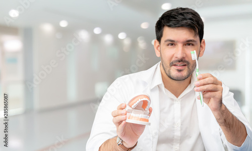 Young male dentist showing toothbrush and denture in dental clinic. Selective focus at the toothbrush. photo