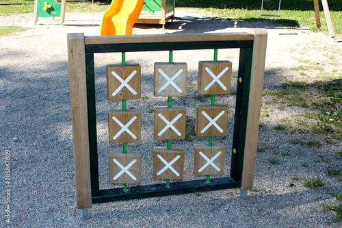 Retro vintage looking outdoor public playground equipment in shape of large wooden frame with x and 0 tiles used to play popular criss cross children game surrounded with playground sand in local publ photo