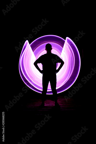 Silhouette of a man standing from the front. Curved abstract shapes made of violet light saber in background. Lightpainting session in long exposure at night. photo