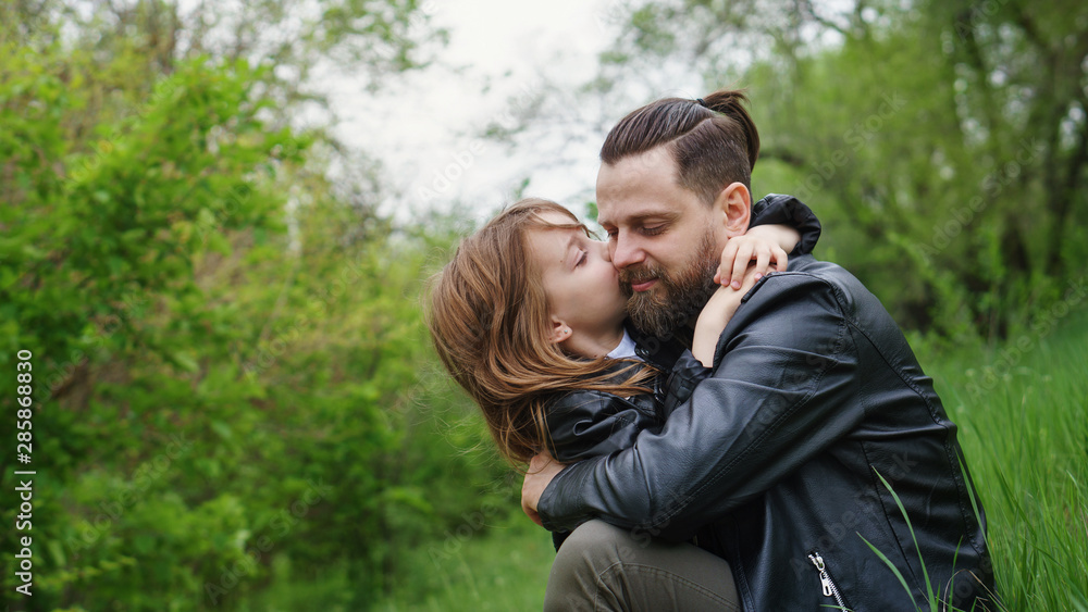 Modern stylish family walking in the park. Daughter hugs and kisses dad.Time together. Family look. Urban casual outfit. Modern stylish family walking in the park. Daughter hugs and kisses dad.Time together. Family look. Urban casual outfit.