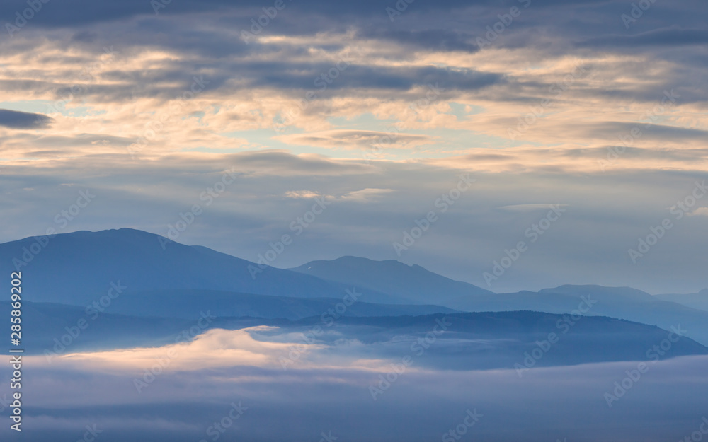 Dawn in the mountains, peaks above the clouds, foggy