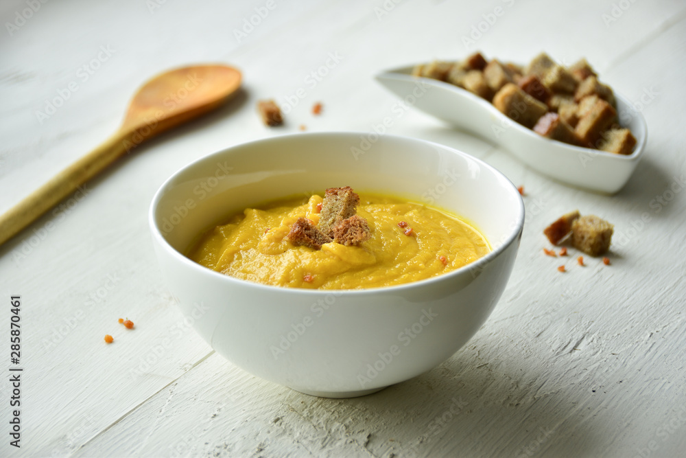 Yellow zucchini and carrot puree soup in a white bowl. White wooden background. Croutons. Yellow zucchini and carrot puree soup in a white bowl. White wooden background. Croutons.