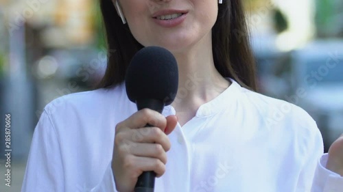 Female newscaster with microphone wireless earphones presenting news, reportage