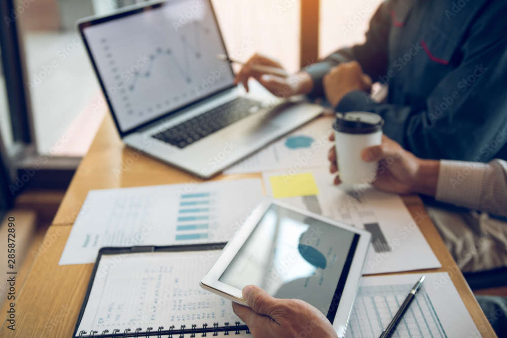 Business partnership pointing to the graph of the company financial statements report and profits earned during in the computer screen with giving a presentation to colleagues holding tablet. Business partnership pointing to the graph of the company financial statements report and profits earned during in the computer screen with giving a presentation to colleagues holding tablet.