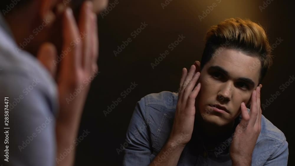 Transgender man looking mirror stroking face, gender identity, transsexualism Transgender man looking mirror stroking face, gender identity, transsexualism