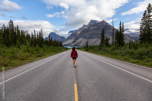 Girl walking down a scenic road in the Canadian Rockies during a vibrant summer evening. Taken in Icefields Parkway, Banff National Park, Alberta, Canada.
