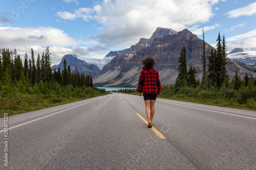 Girl walking down a scenic road in the Canadian Rockies during a vibrant summer evening. Taken in Icefields Parkway, Banff National Park, Alberta, Canada.