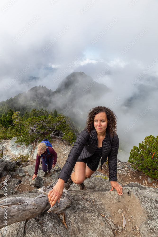 Adventurous Girl is hiking up a steep trail up a beautiful rocky mountain during a cloudy summer morning. Taken on Crown Mountain, North Vancouver, BC, Canada. Adventurous Girl is hiking up a steep trail up a beautiful rocky mountain during a cloudy summer morning. Taken on Crown Mountain, North Vancouver, BC, Canada.