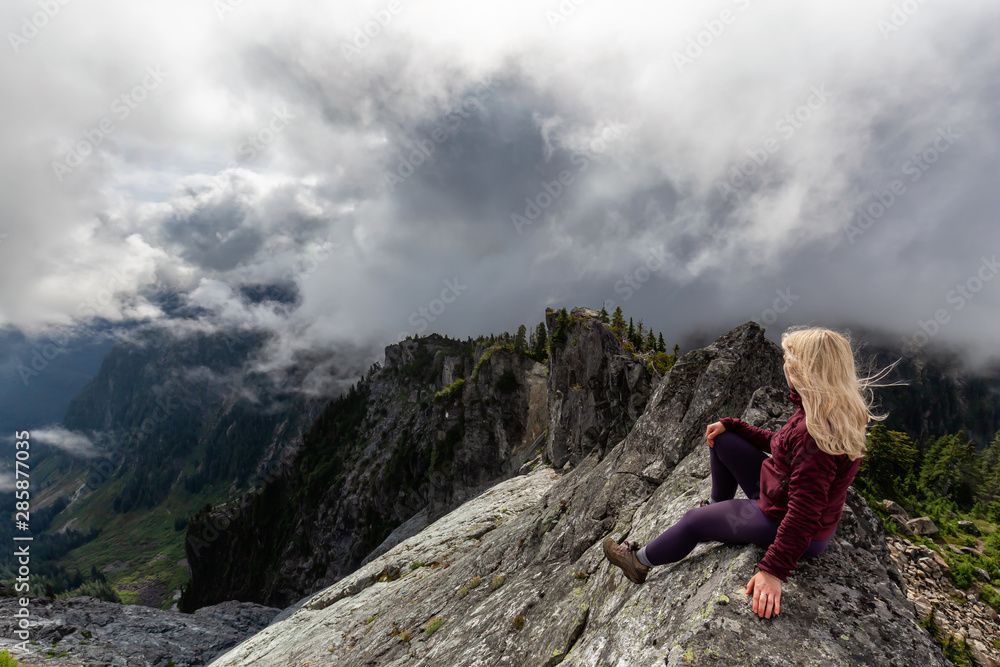 Adventurous Girl on top of a rugged rocky mountain during a cloudy summer morning. Taken on Crown Mountain, North Vancouver, BC, Canada. Adventurous Girl on top of a rugged rocky mountain during a cloudy summer morning. Taken on Crown Mountain, North Vancouver, BC, Canada.