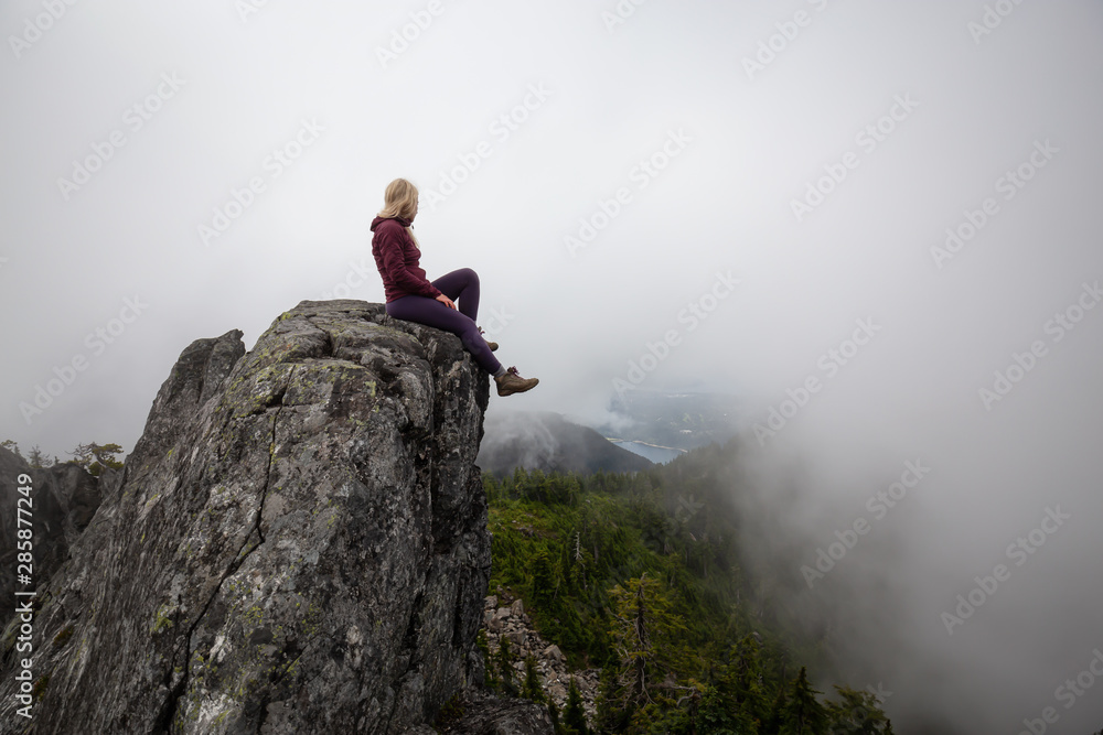 Adventurous Girl on top of a rugged rocky mountain during a cloudy summer morning. Taken on Crown Mountain, North Vancouver, BC, Canada. Adventurous Girl on top of a rugged rocky mountain during a cloudy summer morning. Taken on Crown Mountain, North Vancouver, BC, Canada.
