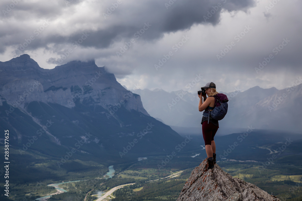 Adventurous Girl taking pictures on top of a rocky mountain during a cloudy and rainy day. Taken from Mt Lady MacDonald, Canmore, Alberta, Canada.