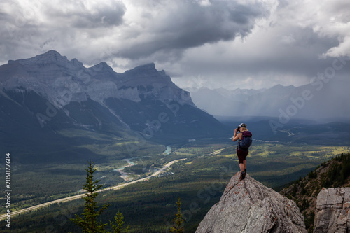 Adventurous Girl taking pictures on top of a rocky mountain during a cloudy and rainy day. Taken from Mt Lady MacDonald, Canmore, Alberta, Canada.