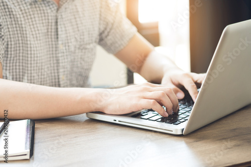 Young college student is typing on laptop keyboard. Internet research concept.