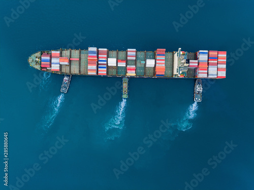 Aerial top view Tugboat pushing container ship to quayside for load/unload container via crane for logistics, import export, shipping or transportation.