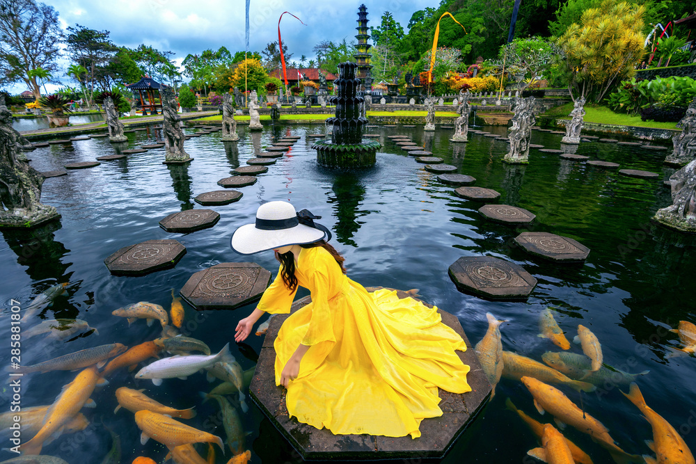 Woman feeding colorful fish in pond at Tirta Gangga Water Palace in Bali,  Indonesia. Photos | Adobe Stock