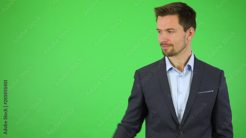 A young handsome businessman takes an invisible point between his fingers and drags it to the other side of the screen, then smiles at the camera - green screen studio A young handsome businessman takes an invisible point between his fingers and drags it to the other side of the screen, then smiles at the camera - green screen studio