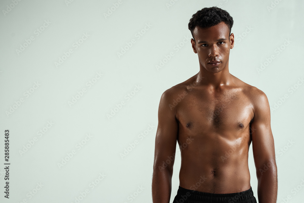 Strong and confident. Portrait of young shirtless muscular african man looking at camera while standing against grey background