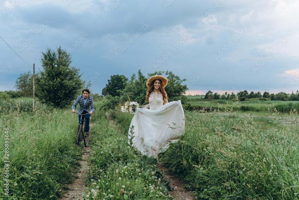 Beautiful young couple bride and groom walking in a field with a bicycle Beautiful young couple bride and groom walking in a field with a bicycle