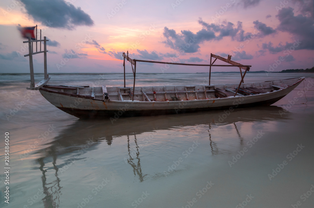Long exposure of a fishing boat on Otres beach at sunset with blurred motion (waves and cambodian flag), Sihanoukville, Cambodia.