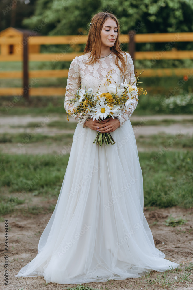 A beautiful young bride with a bouquet of daisies in a field A beautiful young bride with a bouquet of daisies in a field