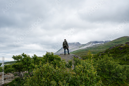 A man stands on top and enjoys a stunning view. Mountain beautiful landscape. Dramatic sky. Enjoy the moment, relax. Wanderlust. Adventure, freedom, lifestyle. Explore North Norway. Summer Scandinavia