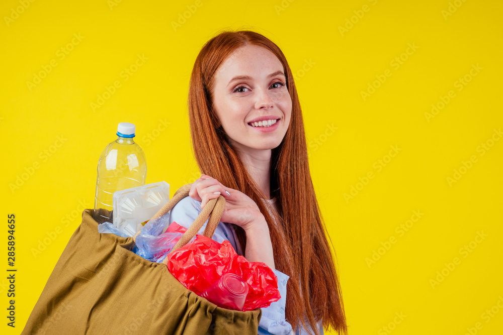 beautiful redhaired ginder happy woman holding cotton eco bag with sorting recycle trash:plastic bottle,disposable package in studio yellow background beautiful redhaired ginder happy woman holding cotton eco bag with sorting recycle trash:plastic bottle,disposable package in studio yellow background