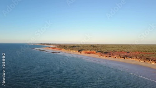 Scenic panoramic aerial drone view of outback landscape in remote Western Australia, flying along ocean, rocky cliff coast, with blue sky, sunset and horizon on a summer sunny day.