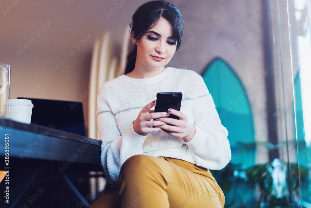 Portrait of girl sitting cafe, using smartphone. Young woman reads text message on phone while sitting coffee shop. Lifestyle. Portrait of girl sitting cafe, using smartphone. Young woman reads text message on phone while sitting coffee shop. Lifestyle.