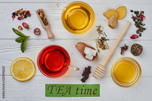 Tea time concept. Flat lay composition with two cups of tea, honey, ginger, lemon and dried tea leaves on white wooden background.