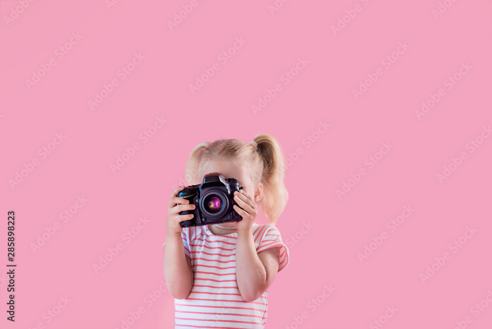 Little pretty girl photographer on pink background shooting with professional photo camera - obrazy, fototapety, plakaty 