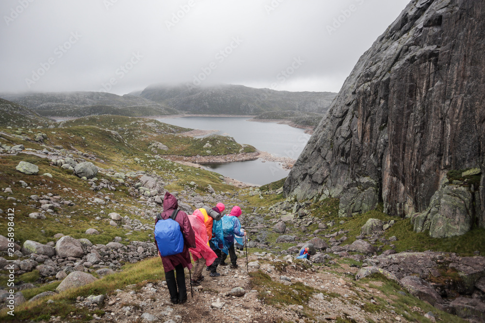 A group of hikers descends from the mountain, lakes are visible in the distance. Hiking in Norway