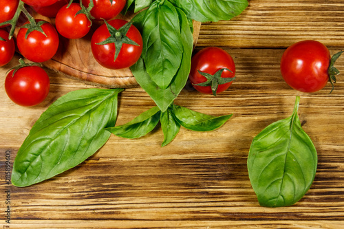 Fresh cherry tomatoes with green basil leaves on a wooden table. Top view