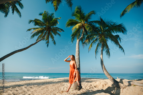 Slim young woman sittng on palm tree, summer background with palms an blue ocean. Vacation in Sri Lanka