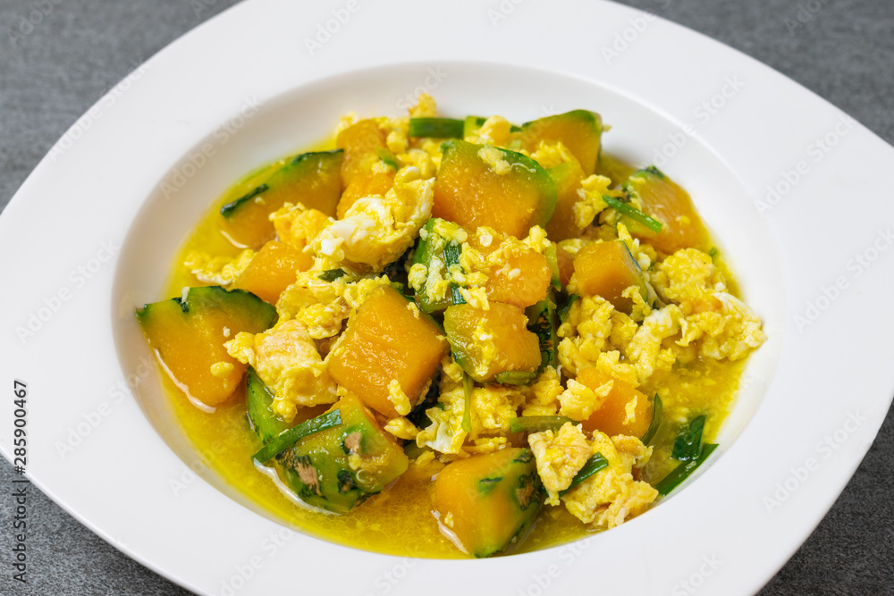 Fried pumpkin with egg for children in white dish on concrete table. Fried pumpkin with egg for children in white dish on concrete table.