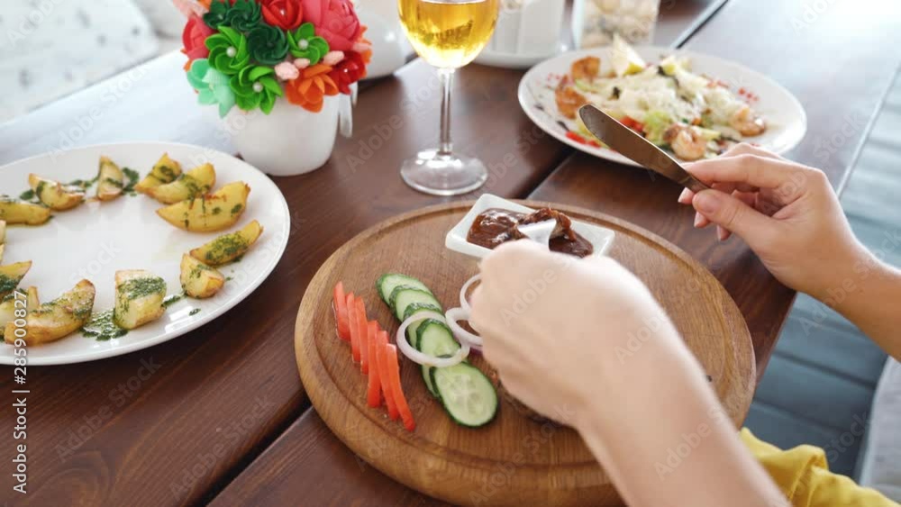 Woman hands holding knife and fork cutting grilled beef steak on wooden plate eat with steak side dish and sauce for dinner meal in restaurant. Lifistyle concept. Videoshot of people on vacation. Woman hands holding knife and fork cutting grilled beef steak on wooden plate eat with steak side dish and sauce for dinner meal in restaurant. Lifistyle concept. Videoshot of people on vacation.