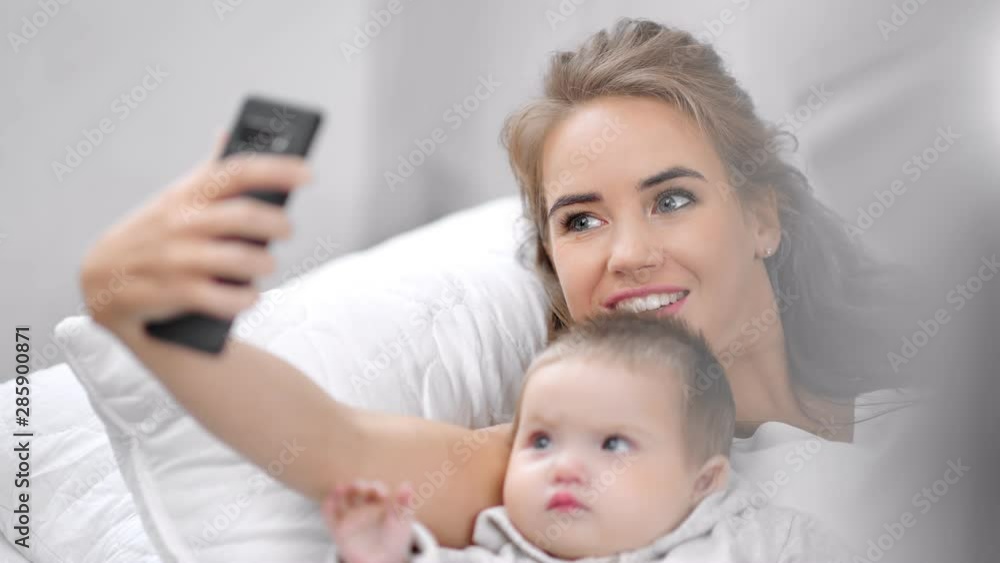 Smiling attractive young mother taking selfie posing with cute baby using smartphone close-up Smiling attractive young mother taking selfie posing with cute baby using smartphone close-up
