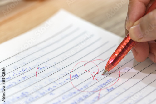 Concept of measurement and evaluation. Hand of teacher using red pen written grade A and circle on math exam paper on wood desk.