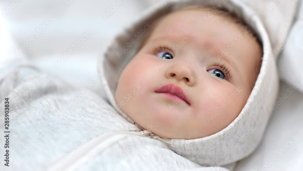 Close-up face of cute little newborn European baby wearing white overall having calmness emotion Close-up face of cute little newborn European baby wearing white overall having calmness emotion