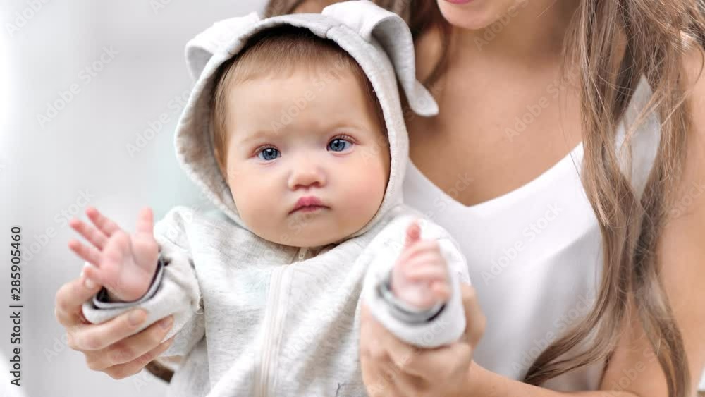 Close-up portrait of newborn cute baby posing sitting on mother knee playing clapping hand Close-up portrait of newborn cute baby posing sitting on mother knee playing clapping hand