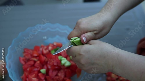 Woman is preparing salad from fresh vegetables. She is cutting tomatoes and cucumber wet hands in the kitchen, hands closeup. photo