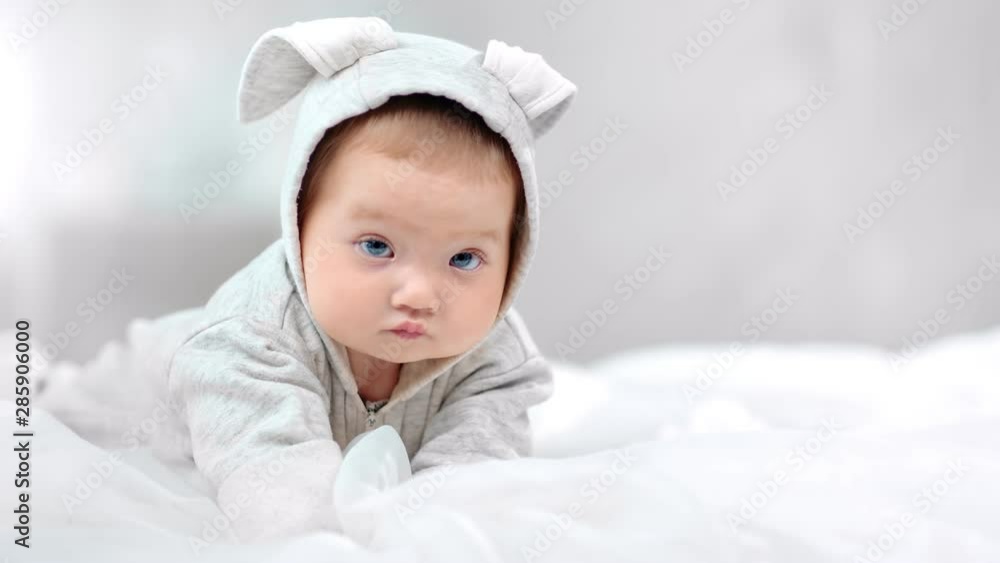 Sweet little baby wearing cute overall posing lying on bed surrounded by morning light Sweet little baby wearing cute overall posing lying on bed surrounded by morning light
