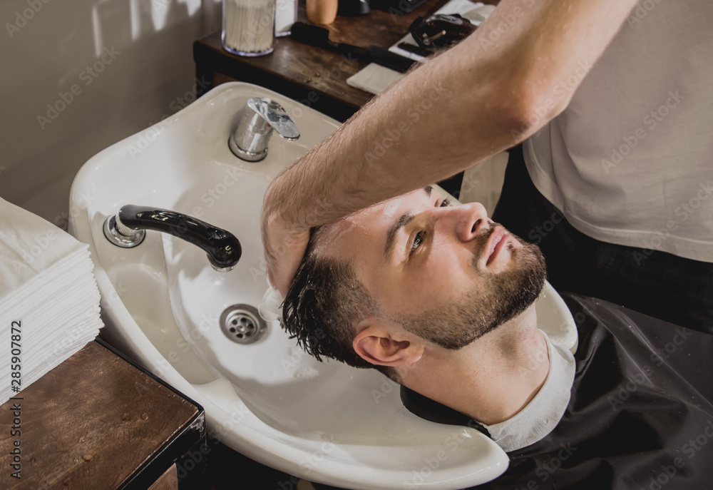 Young man with trendy haircut at barber shop. Barber washes customer head. Young man with trendy haircut at barber shop. Barber washes customer head.