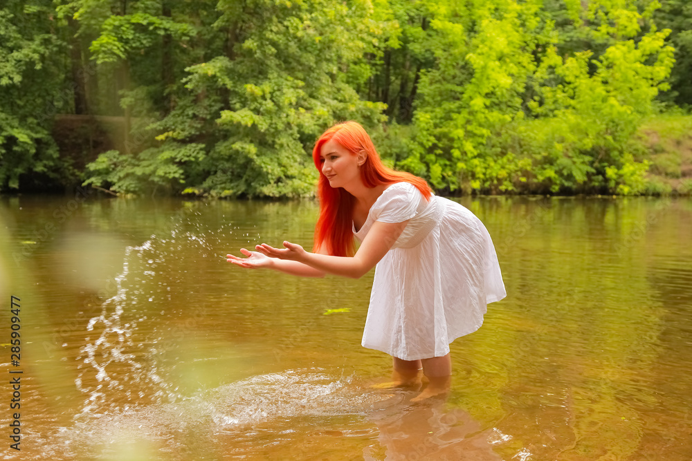 happy redheaded woman in white dress at a river having fun and splashing water in summer. happy person plays with water happy redheaded woman in white dress at a river having fun and splashing water in summer. happy person plays with water