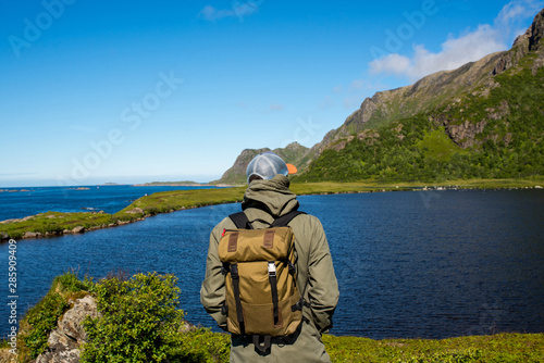 A man with backpack enjoys landscape. Mountain and ocean. Scenic view. Beautiful nature. Green grass, blue sky. Outdoor leisure activity, hiking. Wanderlust. Adventure, lifestyle. Explore North Norway © Iuliia Pilipeichenko