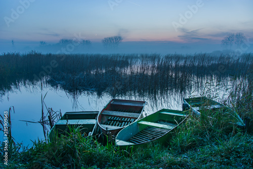 Boats on the shore, reeds and foggy lake
