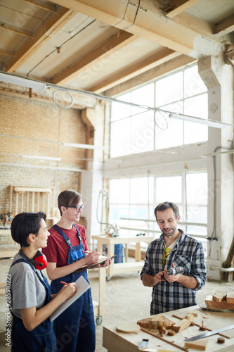 Waist up portrait of mature carpenter teaching young apprentices in workshop, copy space