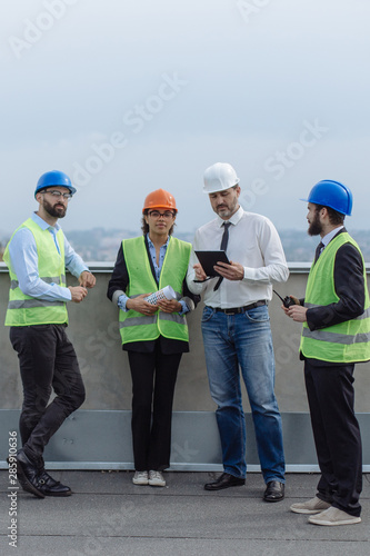 Multiethnic group of workers engineers architects foreman analyzing the plan of construction site on the rooftop of modern building.