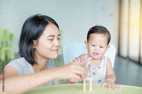 Mom and little baby boy playing wood blocks tower game for Brain and Physical development skill in a classroom. Focus at children face. Child learning and mental skills concept.