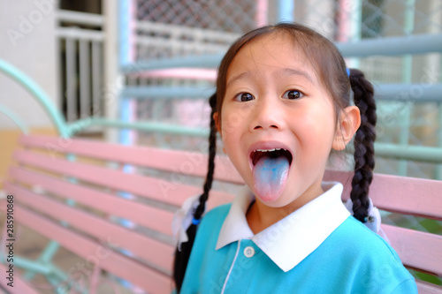 Funny face little Asian child girl smile and poking out blue colored tongue. Food coloring in children sweets. photo