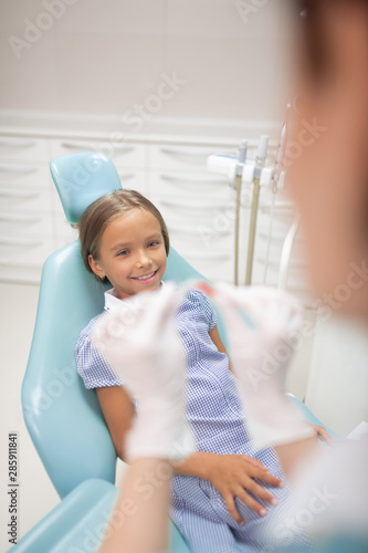 Girl smiling while sitting in dental chair and waiting for mouth guard